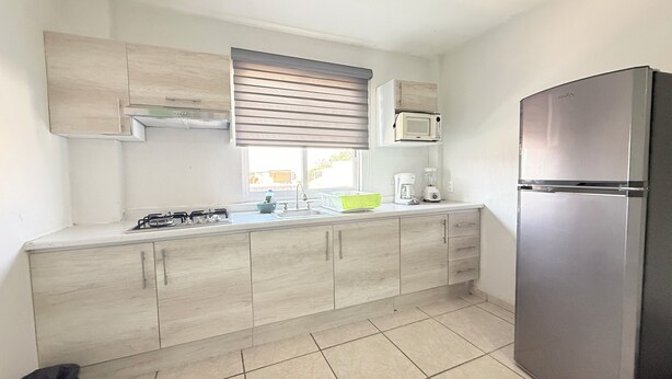 Una cocina con estufa a gas, pileta, microondas, refrigerador y alacenas de madera.