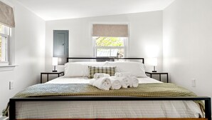 A neatly made bed with rolled towels, a window with a view of trees, and a door to the left. - Crescent Moon: Hot Tub, Arcade, Dogs, EV charger, Minutes from Shenandoah (Luray)
