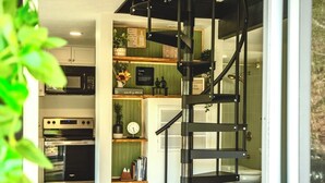 A modern kitchen with a built-in oven and microwave, a black spiral staircase, and a view of the living area. - Crescent Moon: Hot Tub, Arcade, Dogs, EV charger, Minutes from Shenandoah (Luray)
