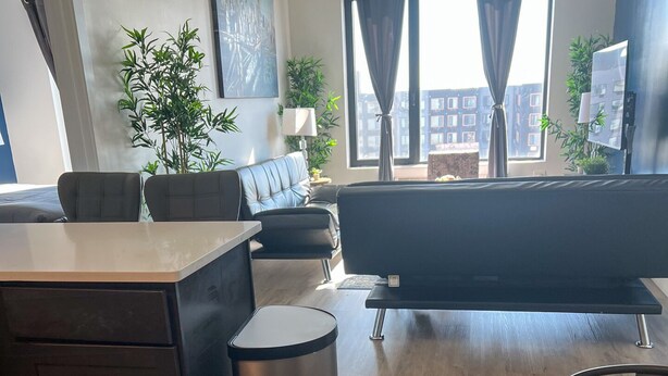 Een moderne woonkamer met een bank, een glazen salontafel en een uitzicht op de stad door grote ramen.