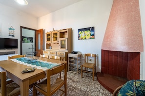 A dining area with a wooden table, chairs, a TV, and a kitchen area with cabinets and a refrigerator.
