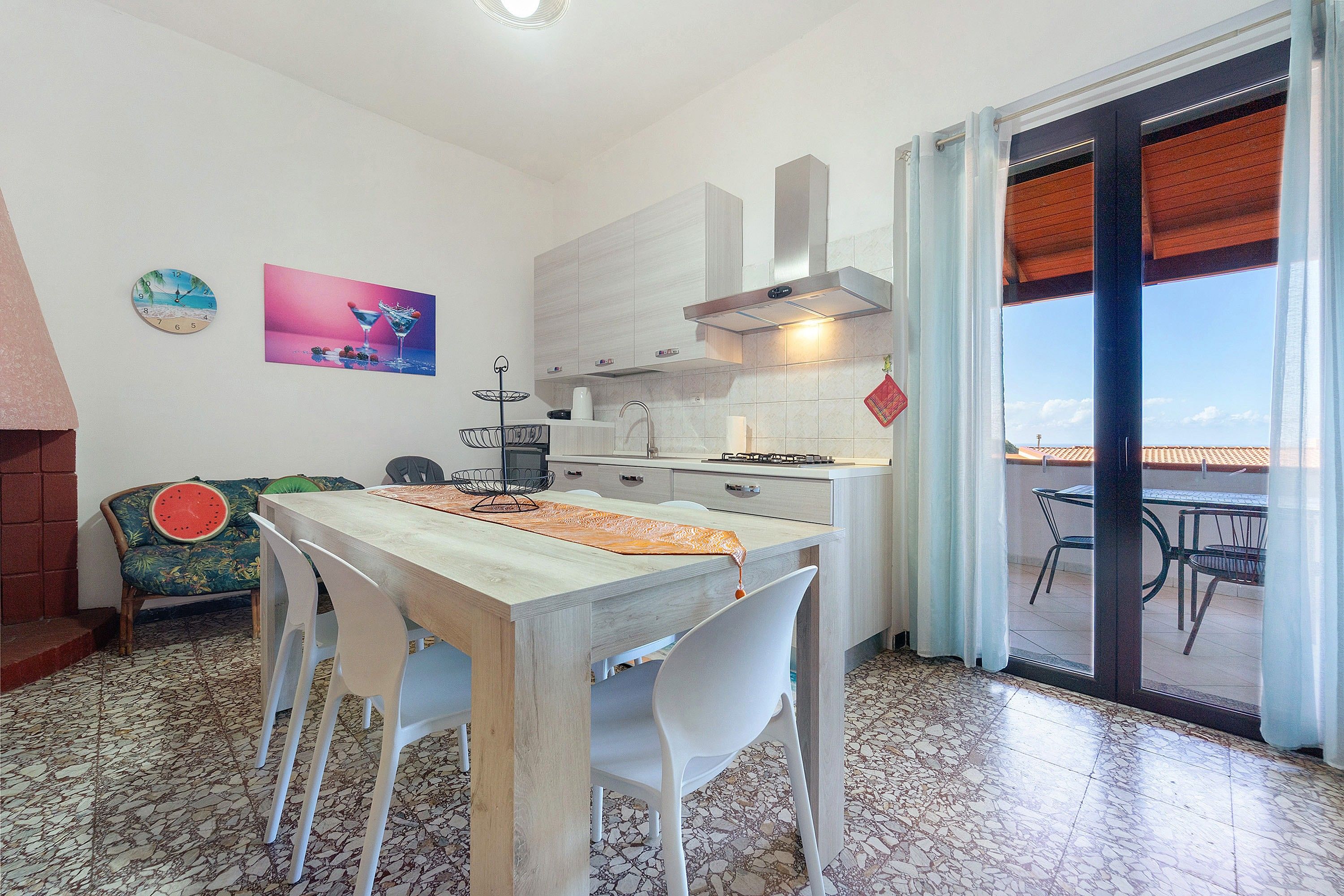 A kitchen with a dining table, chairs, a clock, and a view through a glass door.