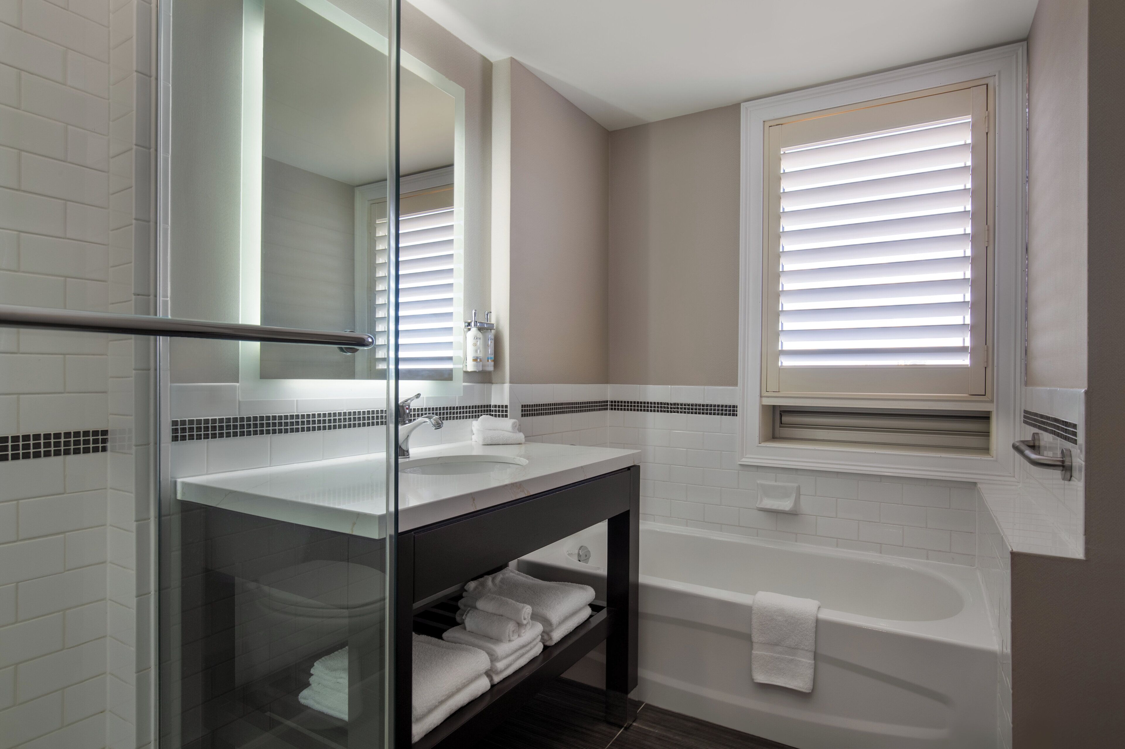 A modern bathroom with a glass shower enclosure, a white sink, a dark vanity, and a bathtub.