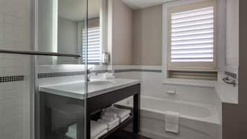 A modern bathroom with a glass shower enclosure, a white sink, a dark vanity, and a bathtub.