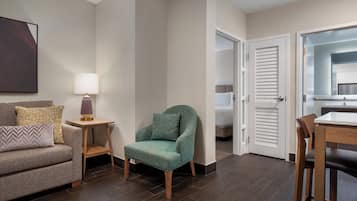 Et hotelværelse med en sofa, en turkis lænestol, et lille bord med en lampe, en træstol og en seng med hvid sengegavl.