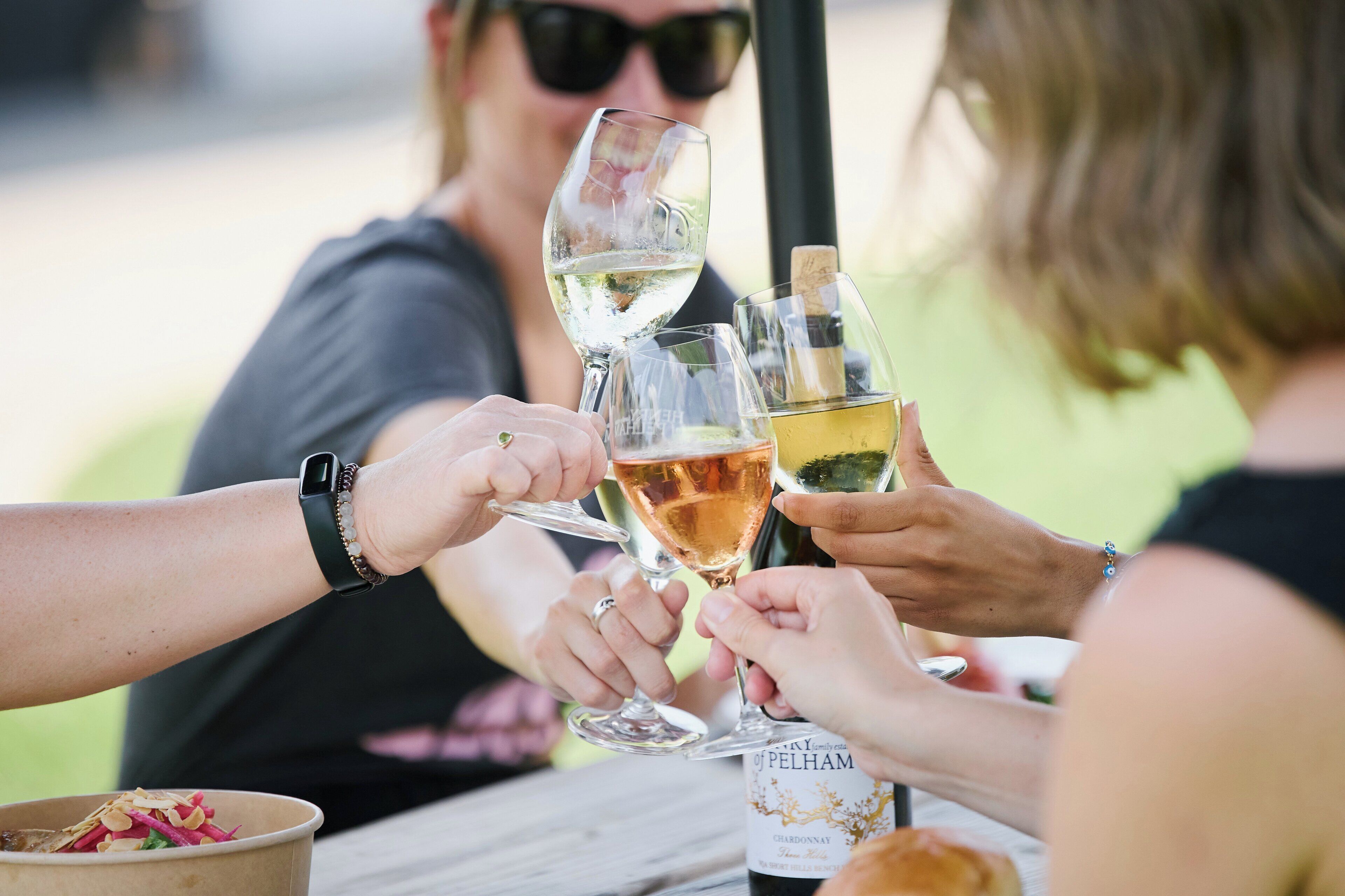 A group of people toasting with wine glasses at a table with a bottle of wine labeled "Pelhamm".