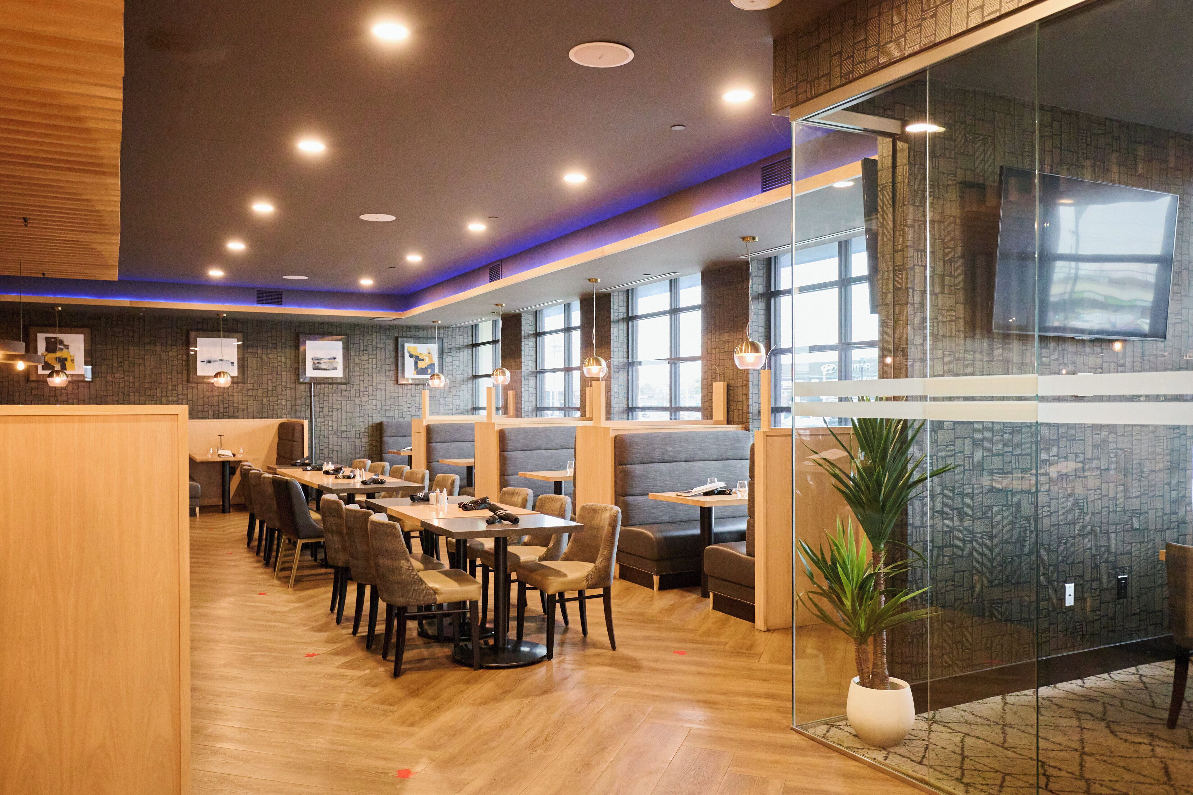 Un restaurante moderno con suelo de madera, varias zonas de estar que incluyen cabinas y mesas, y un amplio ventanal que proporciona luz natural.