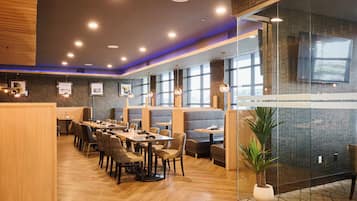 Un restaurante moderno con suelo de madera, varias zonas de estar que incluyen cabinas y mesas, y un amplio ventanal que proporciona luz natural.