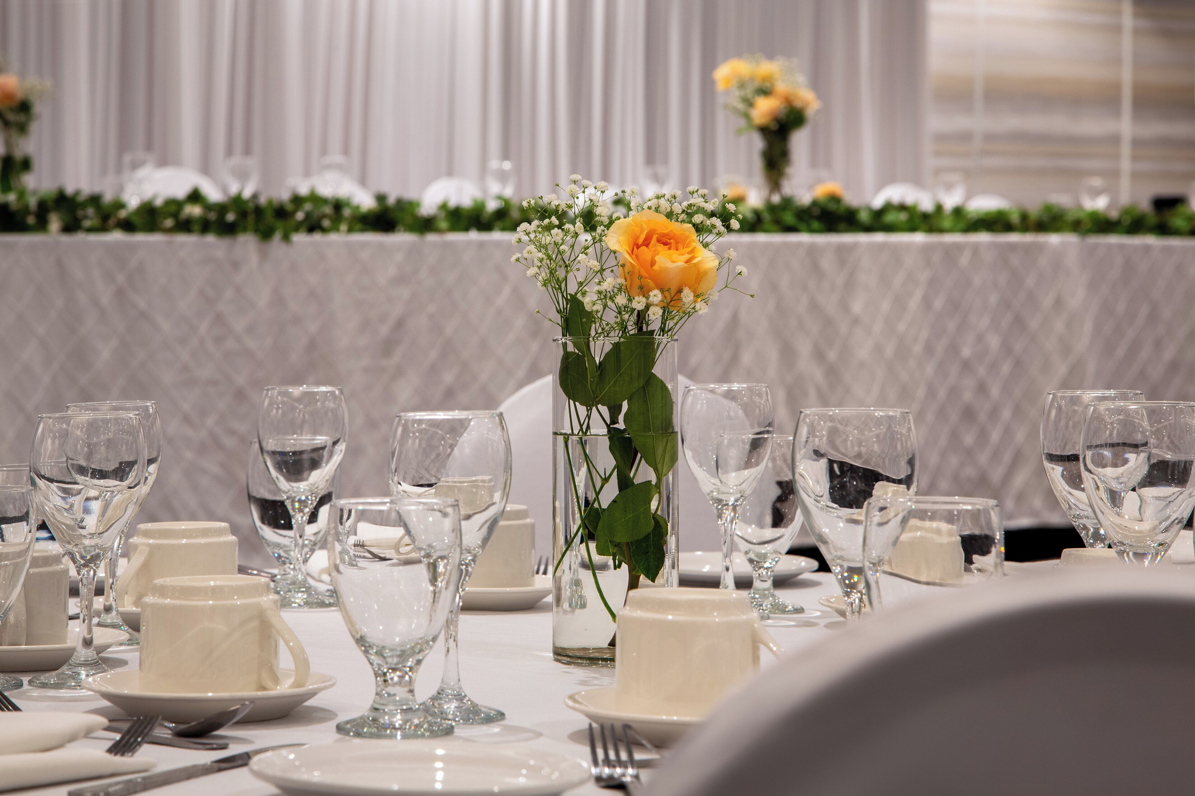 A table set for a formal event with clear glassware, plates, and a centerpiece with a yellow rose.