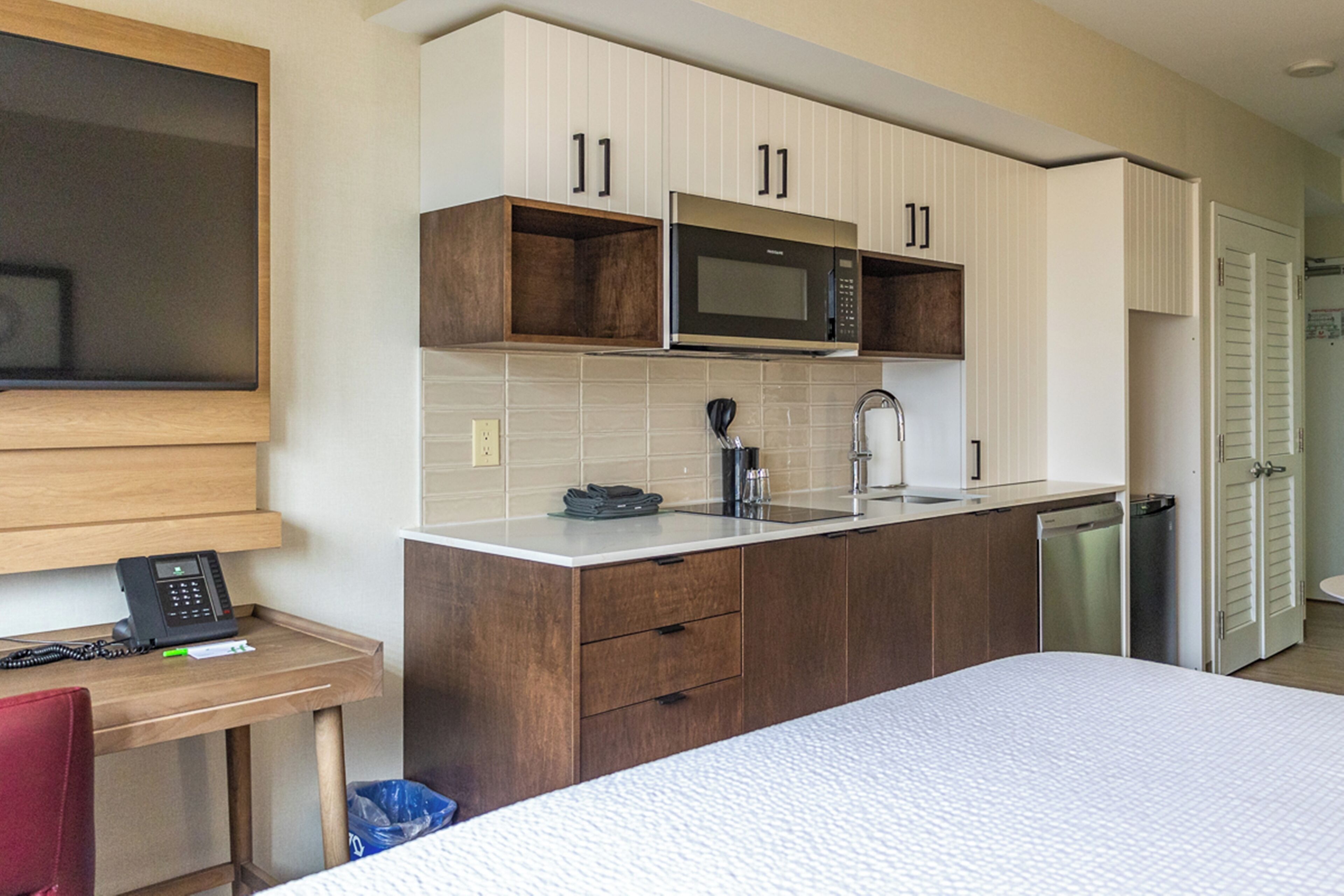 A compact kitchen with a microwave, sink, and cabinets. There's a small table with a phone and trash bin.