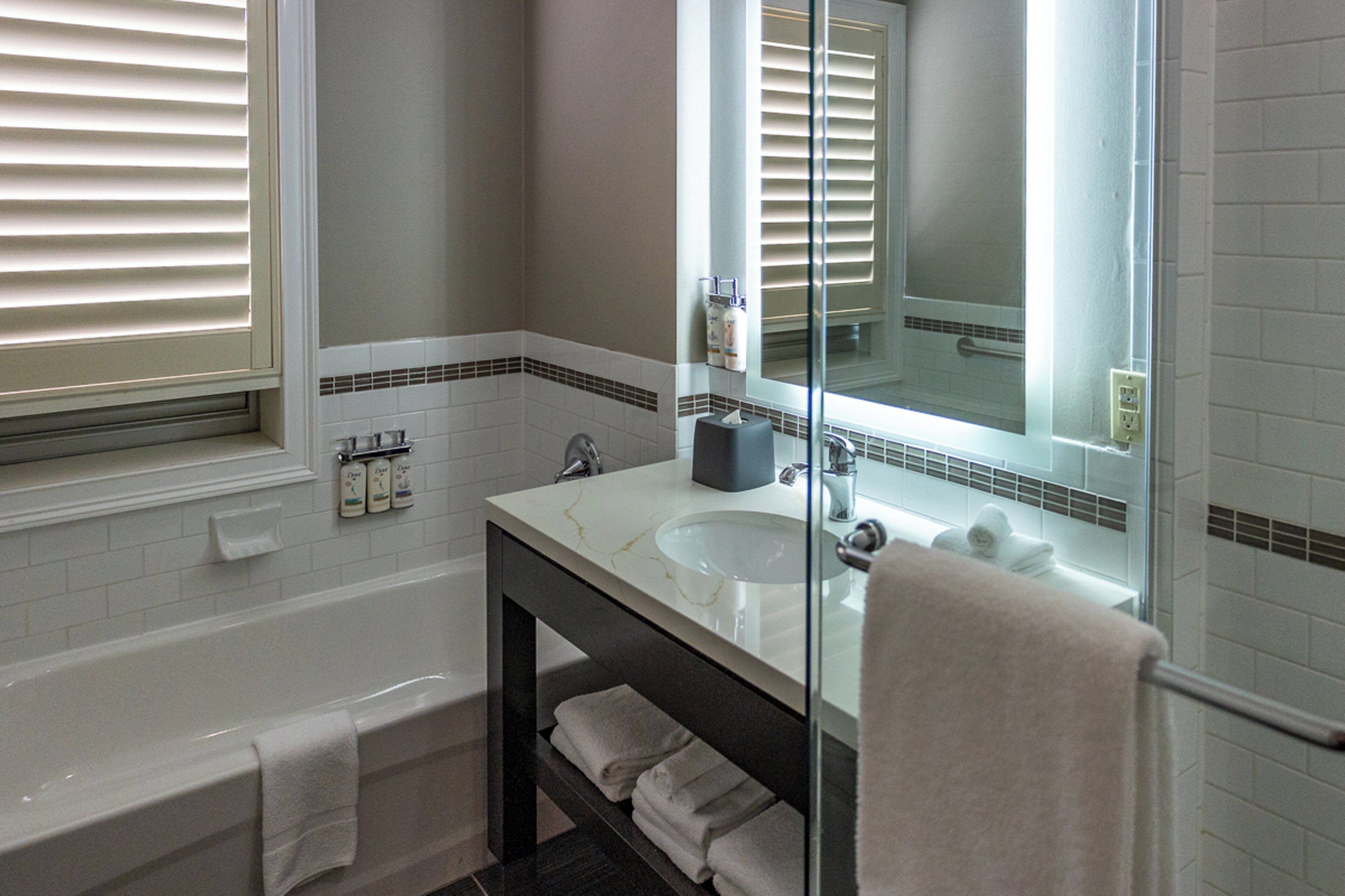 A modern bathroom with a bathtub, a glass-enclosed sink, and a large mirror.