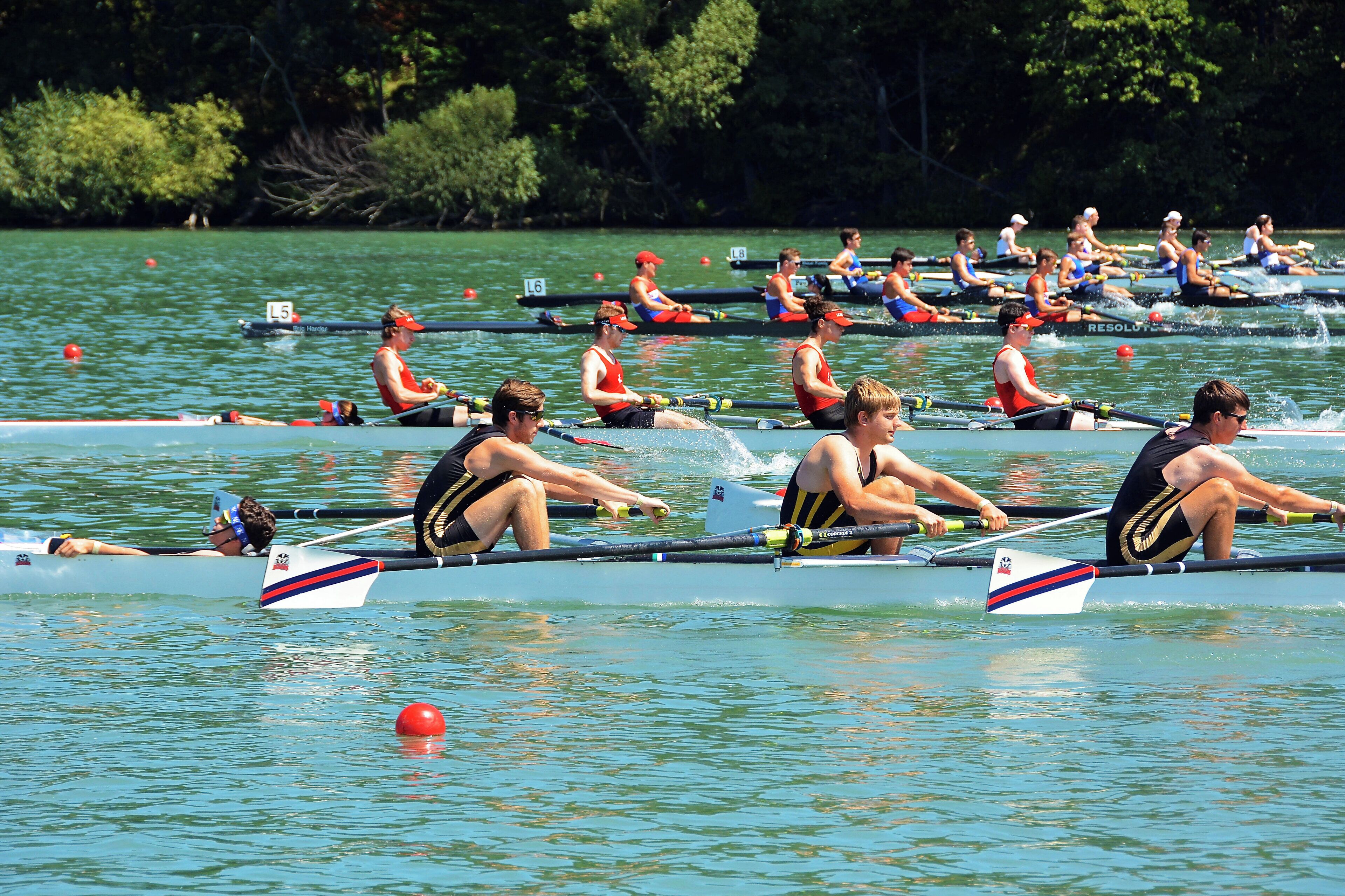 Un equipo de remo compitiendo en una regata en un lago tranquilo, con árboles al fondo.