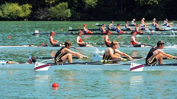 Un equipo de remo compitiendo en una regata en un lago tranquilo, con árboles al fondo.
