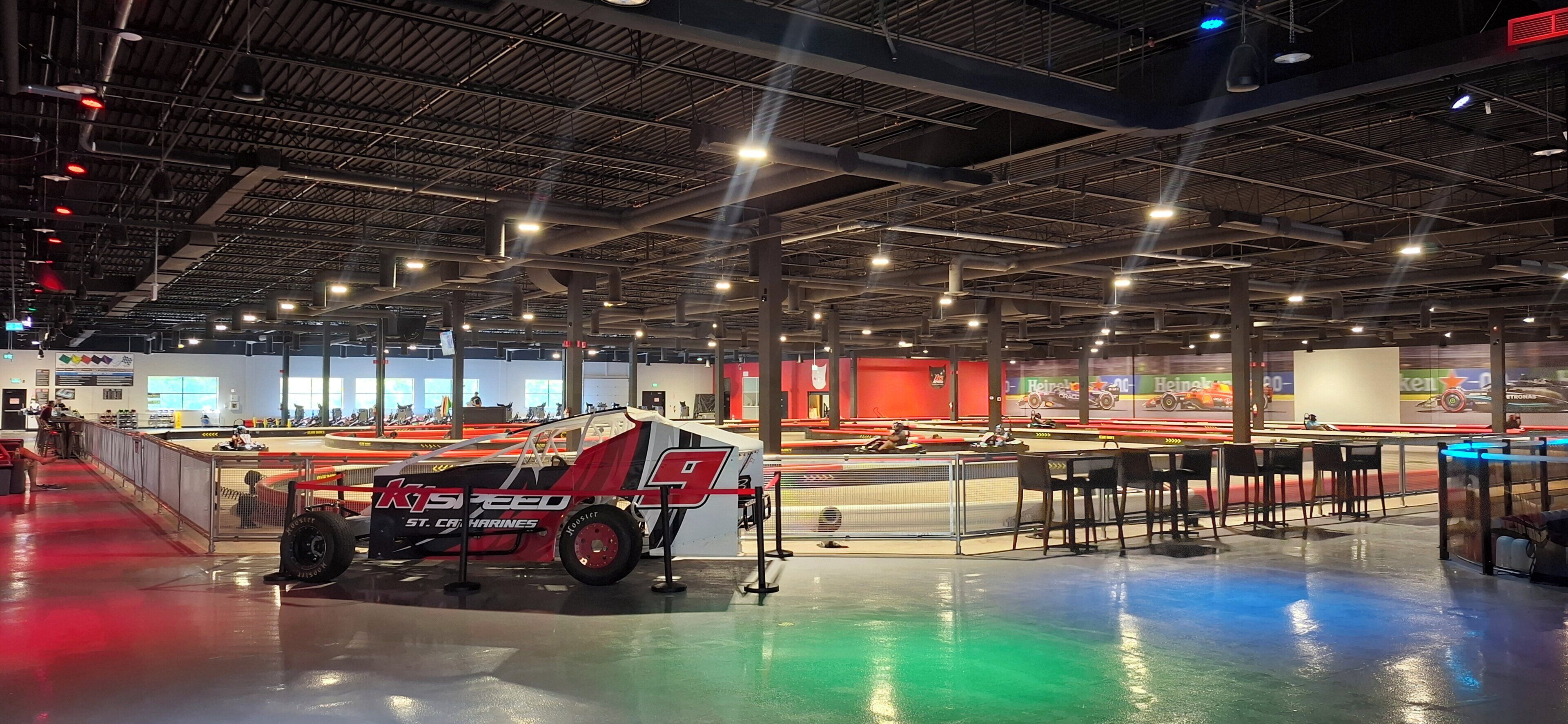 Un vaste espace intérieur comprenant une exposition de voitures de course, des coins salon et un haut plafond avec des poutres apparentes.