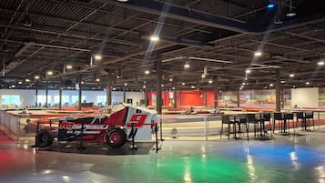 Un vaste espace intérieur comprenant une exposition de voitures de course, des coins salon et un haut plafond avec des poutres apparentes.
