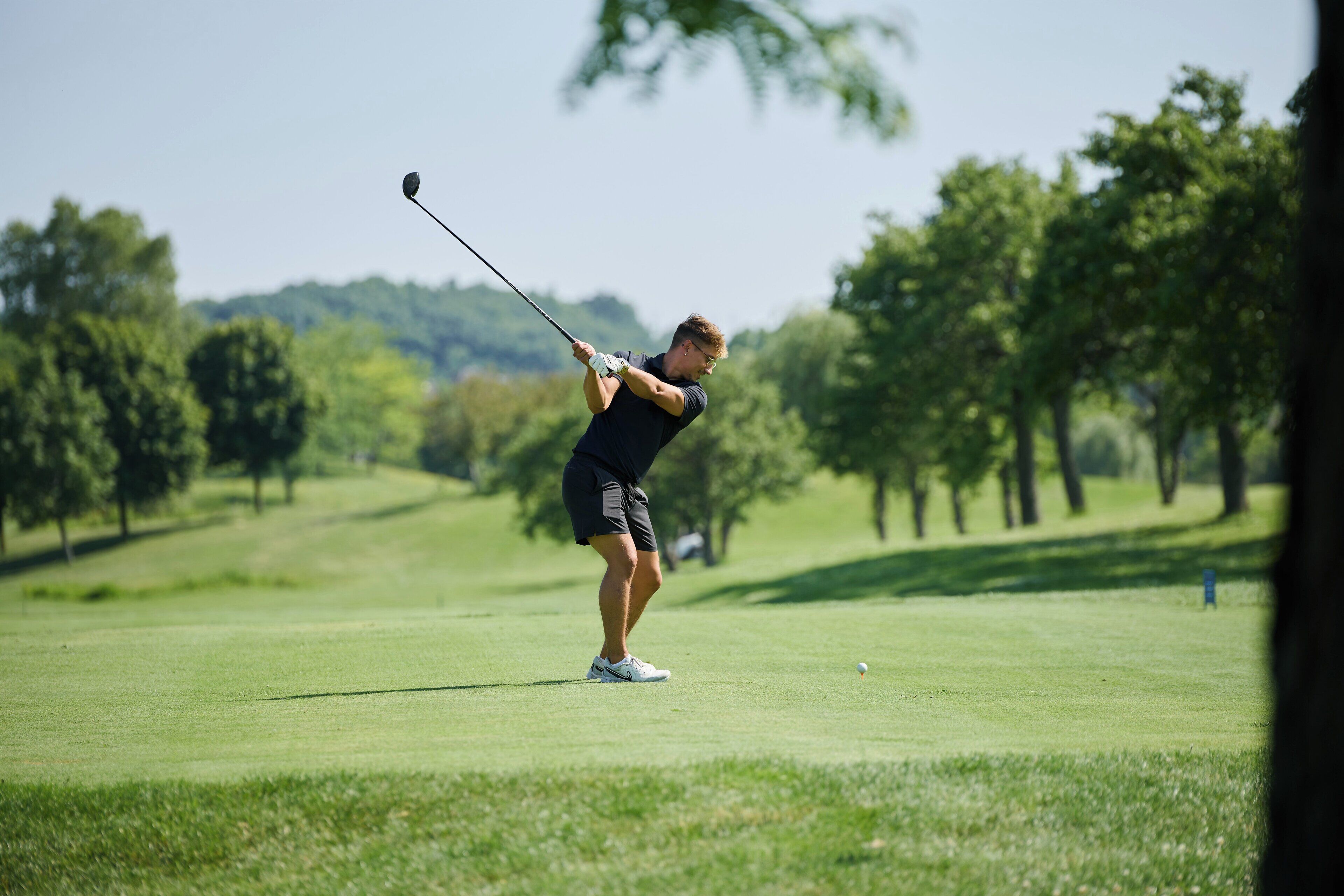 A person playing golf on a well-maintained course with trees in the background.