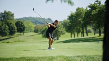 A person playing golf on a well-maintained course with trees in the background.