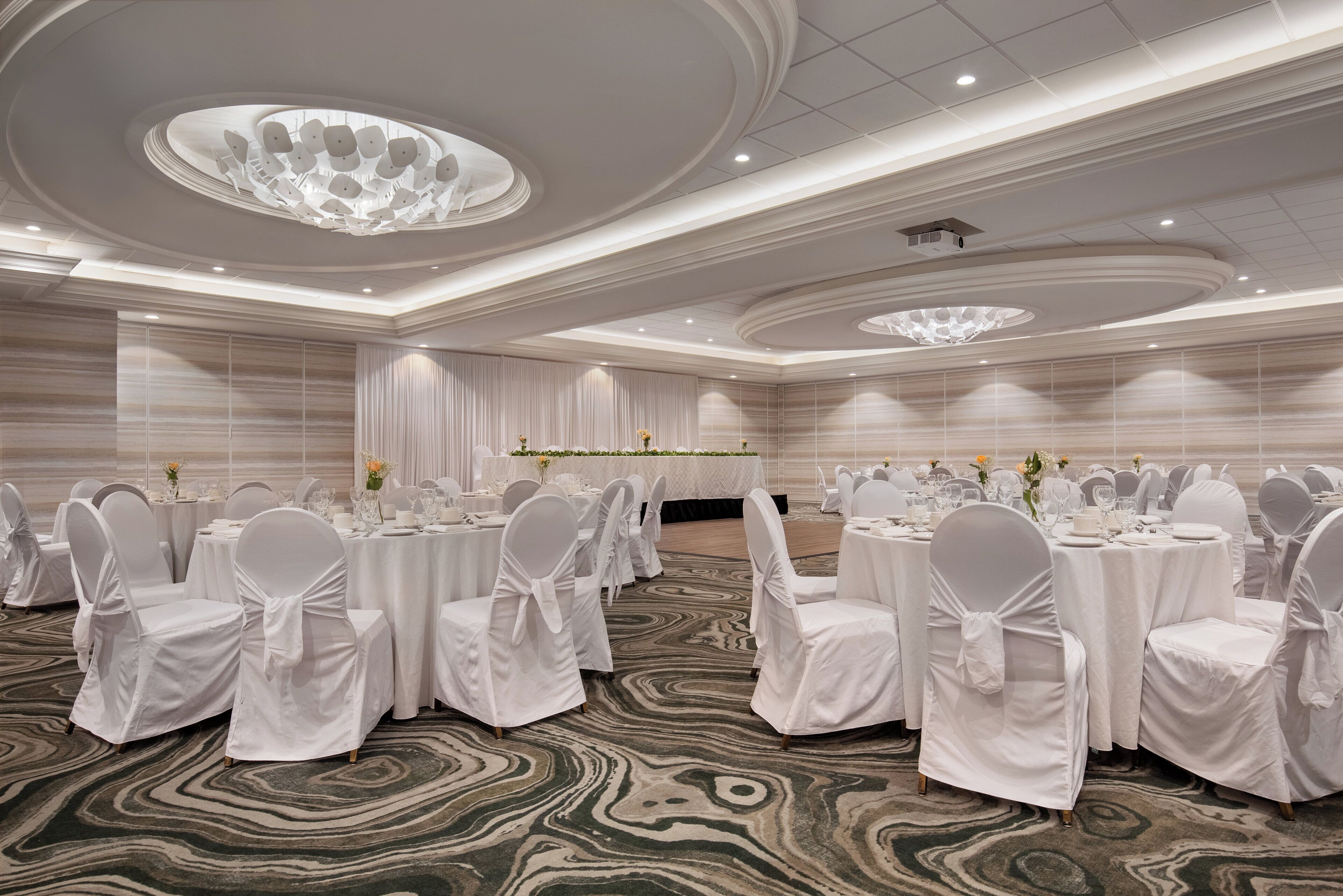 A banquet hall with round tables, white chairs, and a marble-patterned carpet.