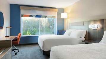 Une chambre d’hôtel avec deux lits, un bureau, une chaise et une grande fenêtre donnant sur la verdure.