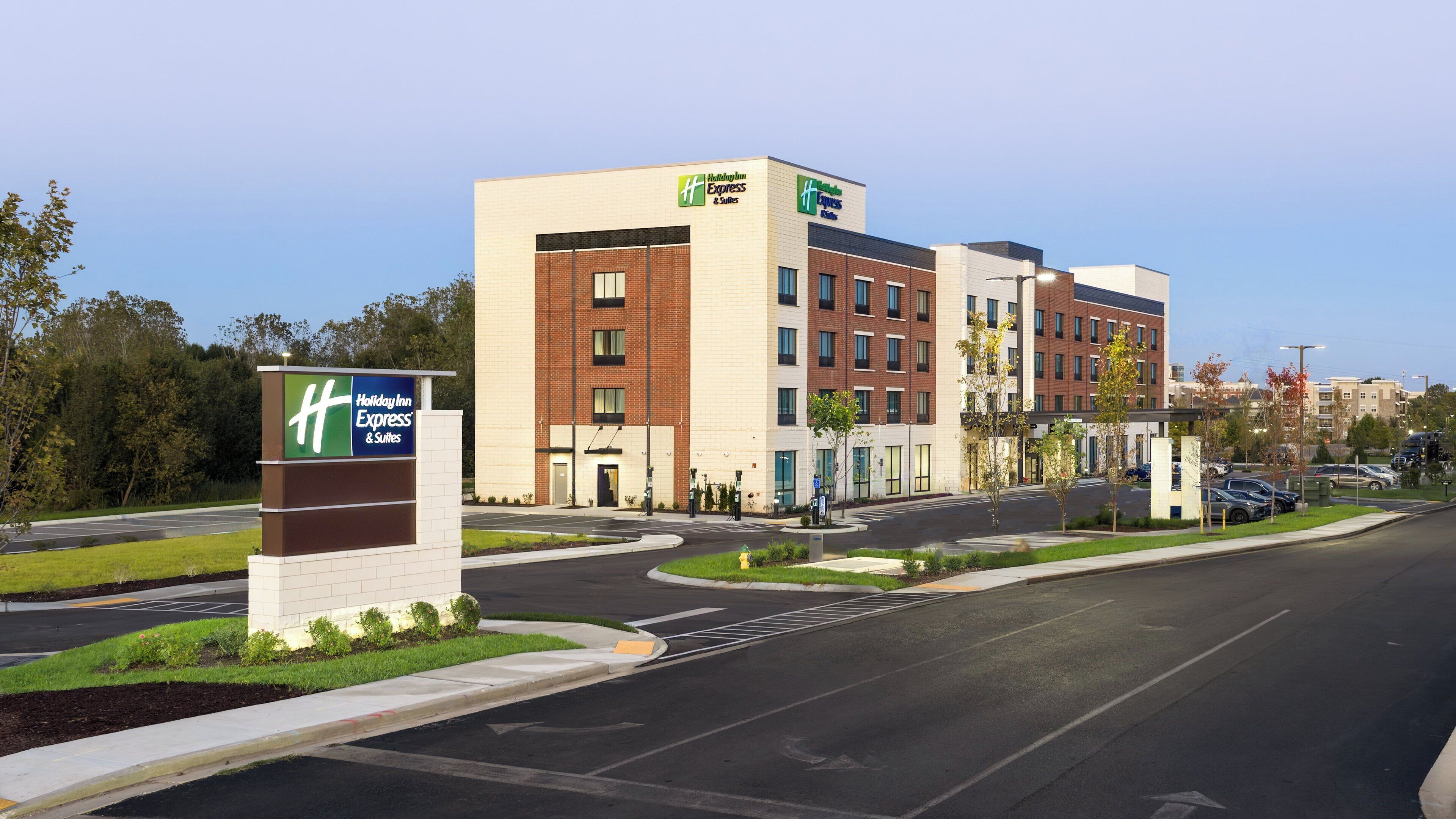 A Holiday Inn Express & Suites building with a modern design, featuring a mix of brick and white exterior walls, multiple windows, and a parking lot with cars.