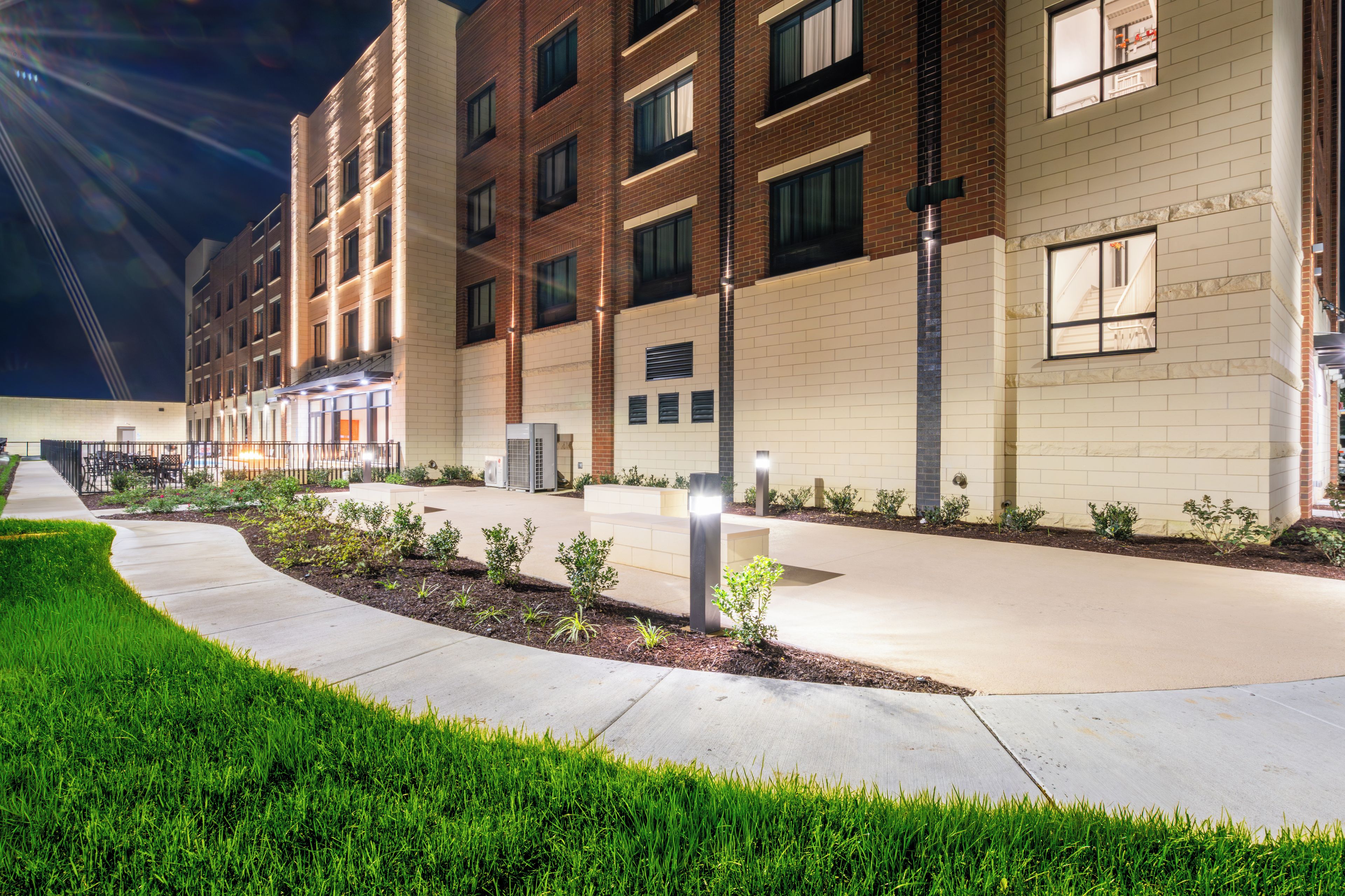 A multi-story building with a brick facade, a landscaped courtyard, and a pathway leading to the entrance.