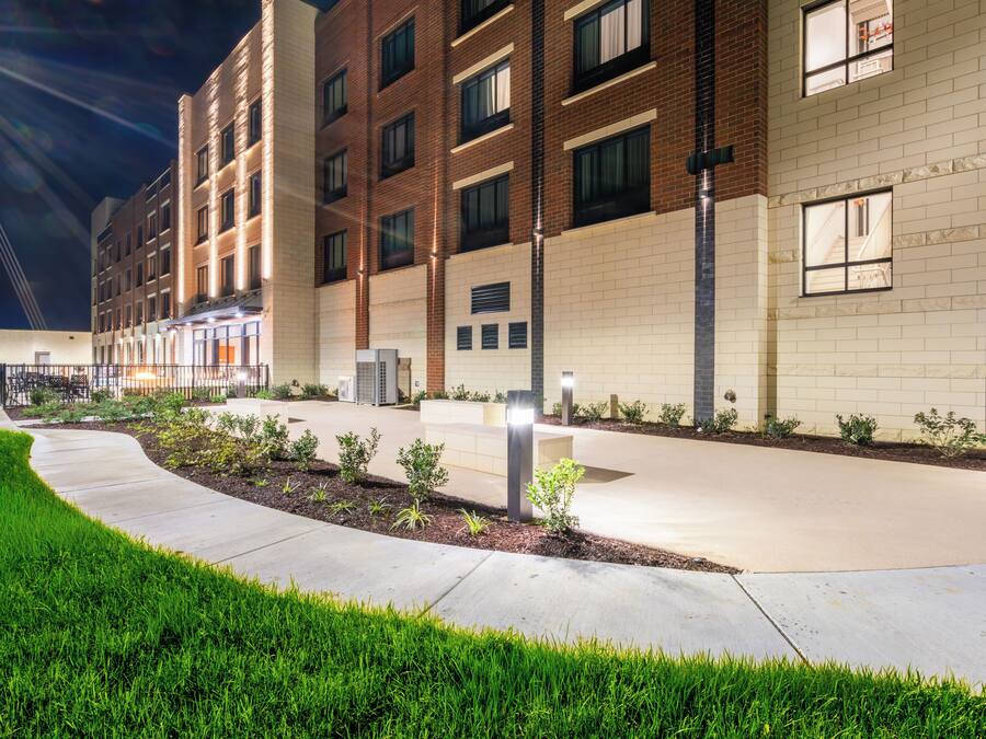 A multi-story building with a brick facade, a landscaped courtyard, and a pathway leading to the entrance.
