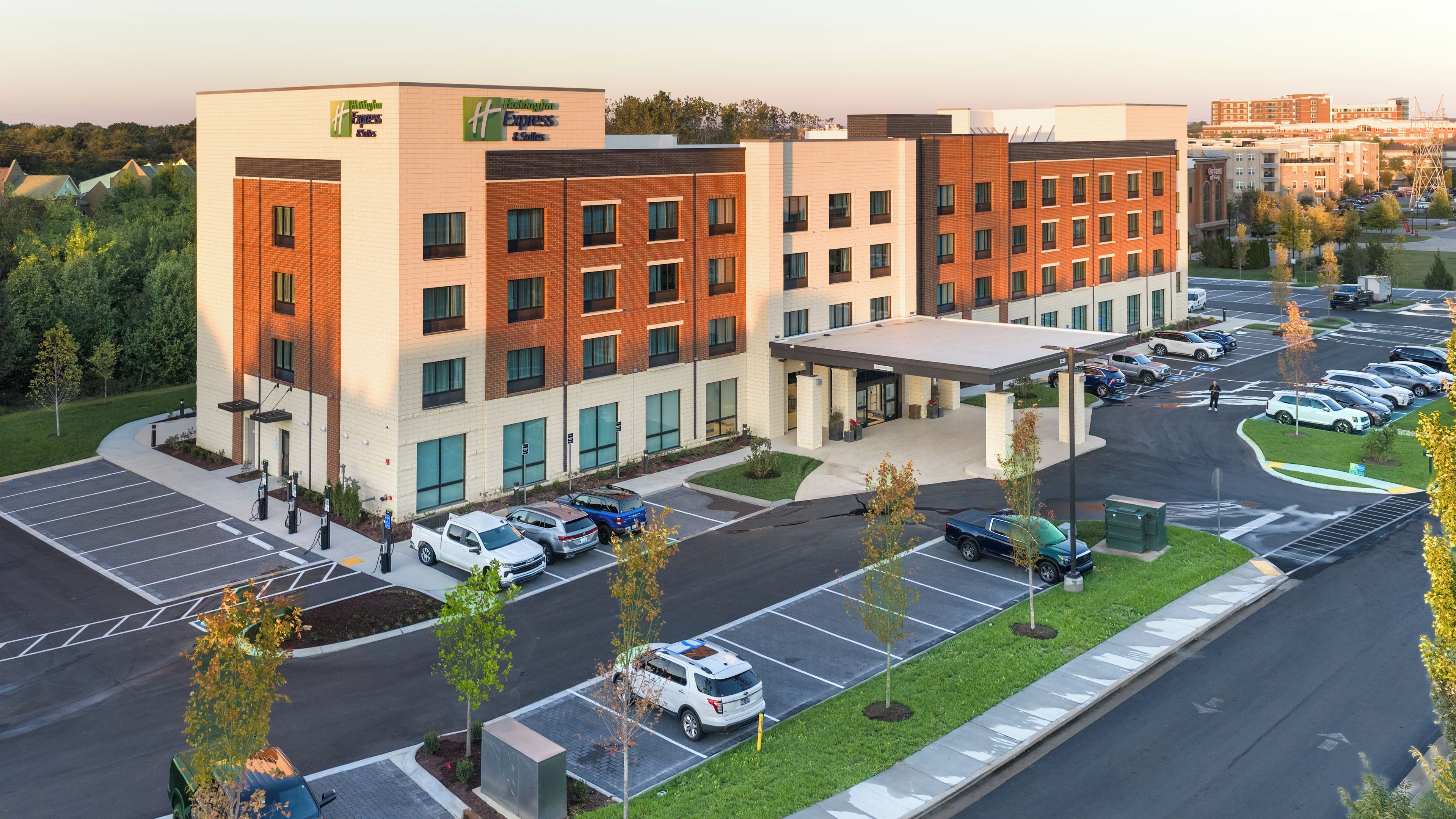 A multi-story hotel with a parking lot, a covered entrance, and a landscaped area with trees.