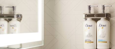 A bathroom with a modern sink, a mirror, and two Dove hand soap dispensers mounted on the wall.
