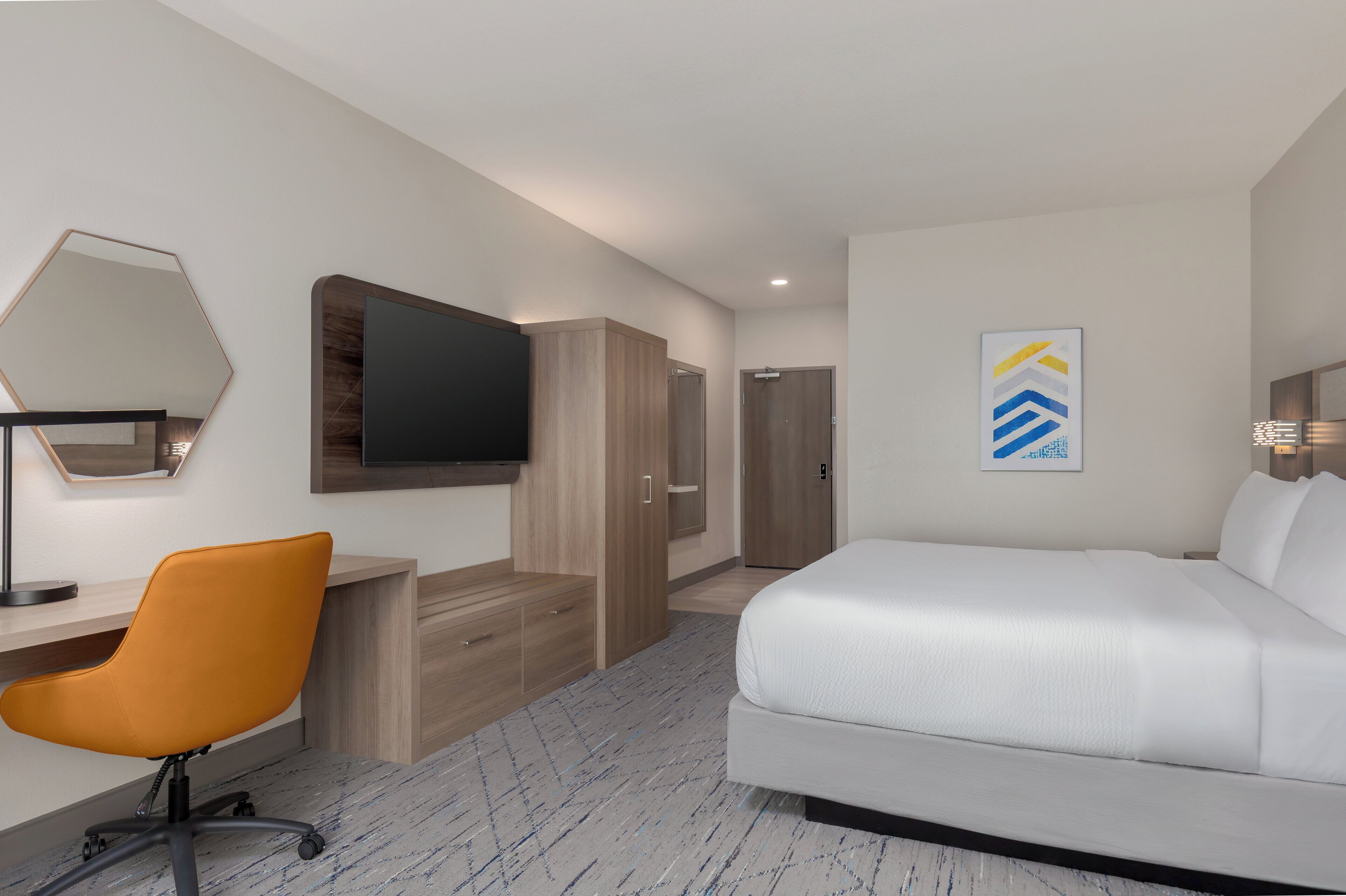 A hotel room with a bed, a desk with a chair, a TV, a wardrobe, and a door.