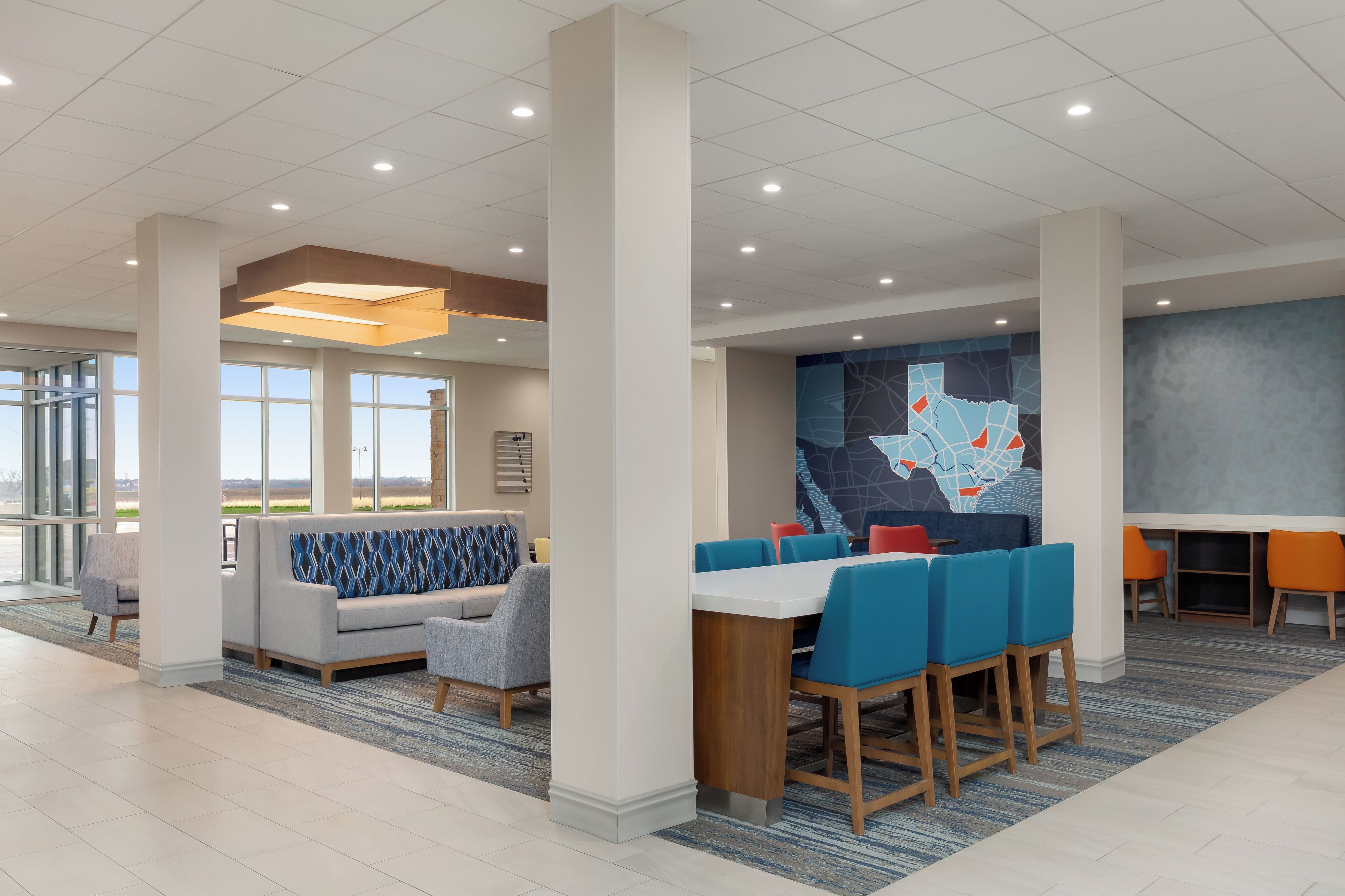 A modern hotel lobby with a seating area, a dining space, and a large wall mural.