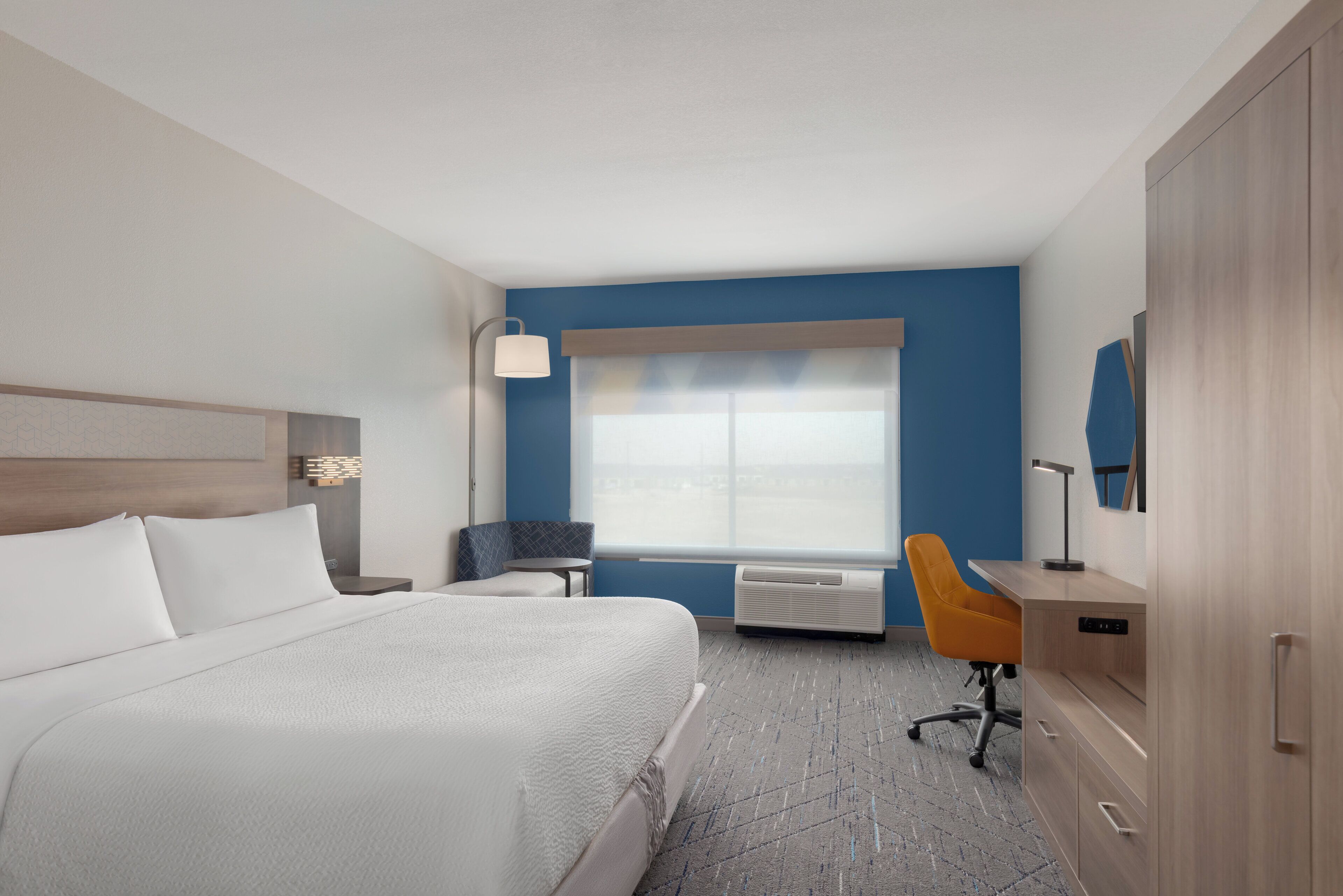 A hotel room with a bed, a desk, an air conditioner, a chair, and a window.