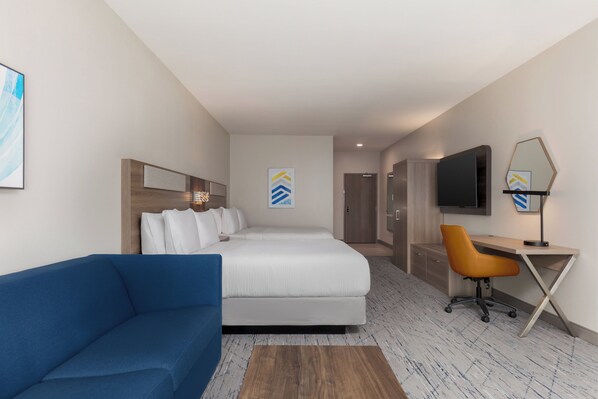 A hotel room with a bed, a blue sofa, a desk with a chair, a TV, and artwork on the walls. - Holiday Inn Express & Suites Prosper South - Frisco by IHG (Prosper)
