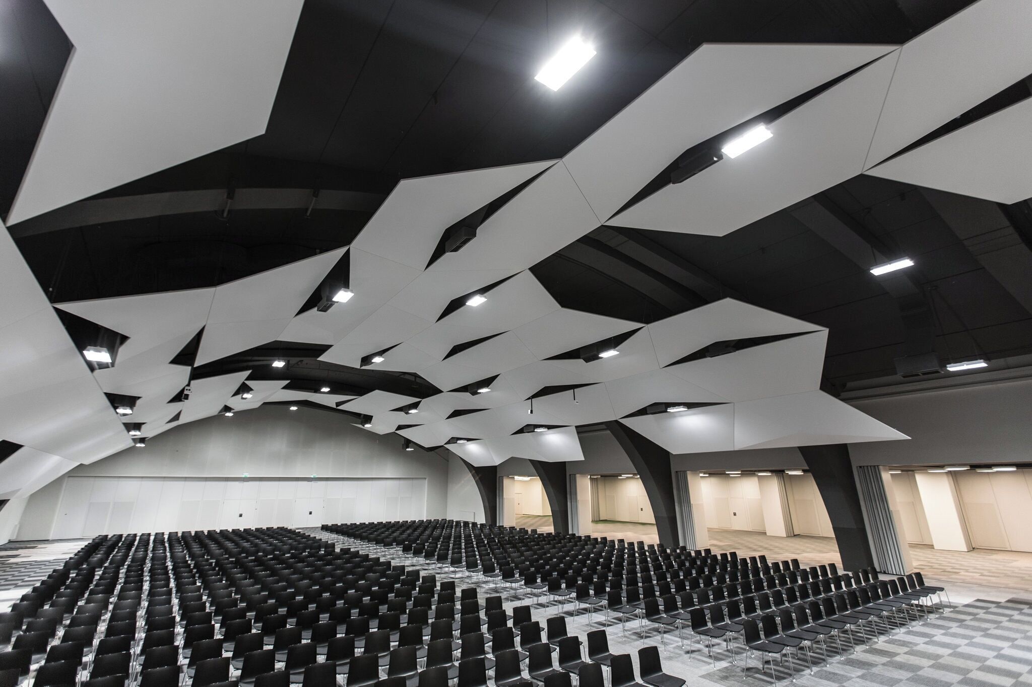 Un salón amplio con filas de sillas y un diseño moderno del techo.