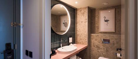 A modern bathroom with a round mirror, a sink, a toilet, and a framed artwork of a flamingo.