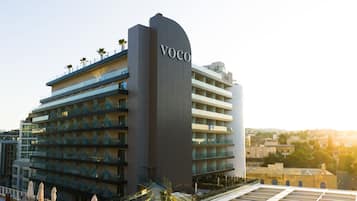 A modern hotel with a prominent 'Voco' sign, multiple balconies, and a rooftop terrace.