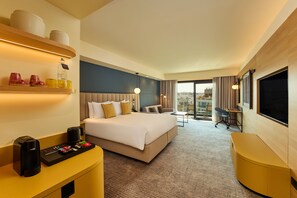 A hotel room with a bed, bedside table, desk, chair, and a large window with a view. - voco Malta by IHG (St. Julian's)