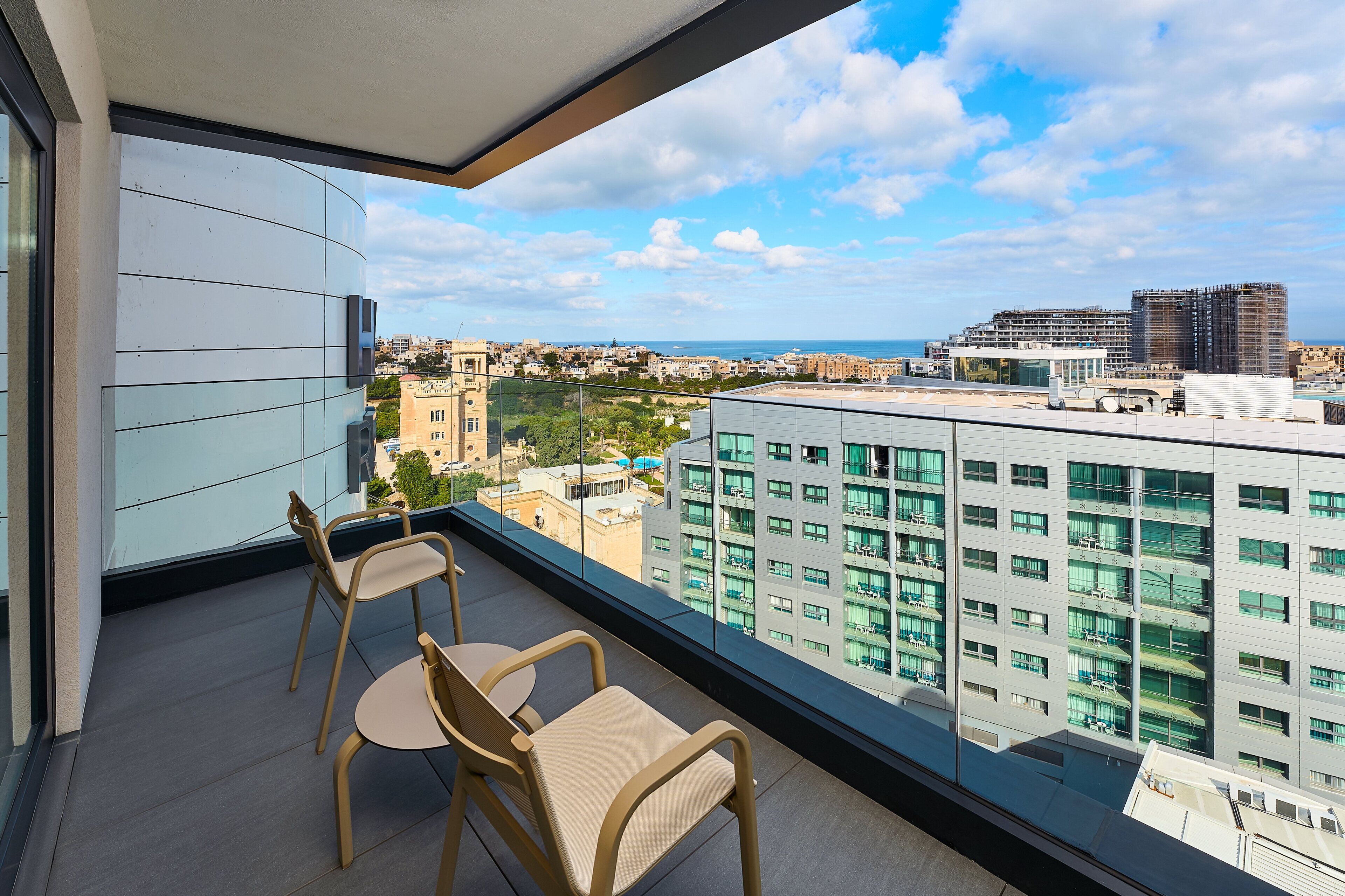 Un balcón con dos sillas y una mesa, con vista a un paisaje urbano con edificios modernos y cielo despejado.