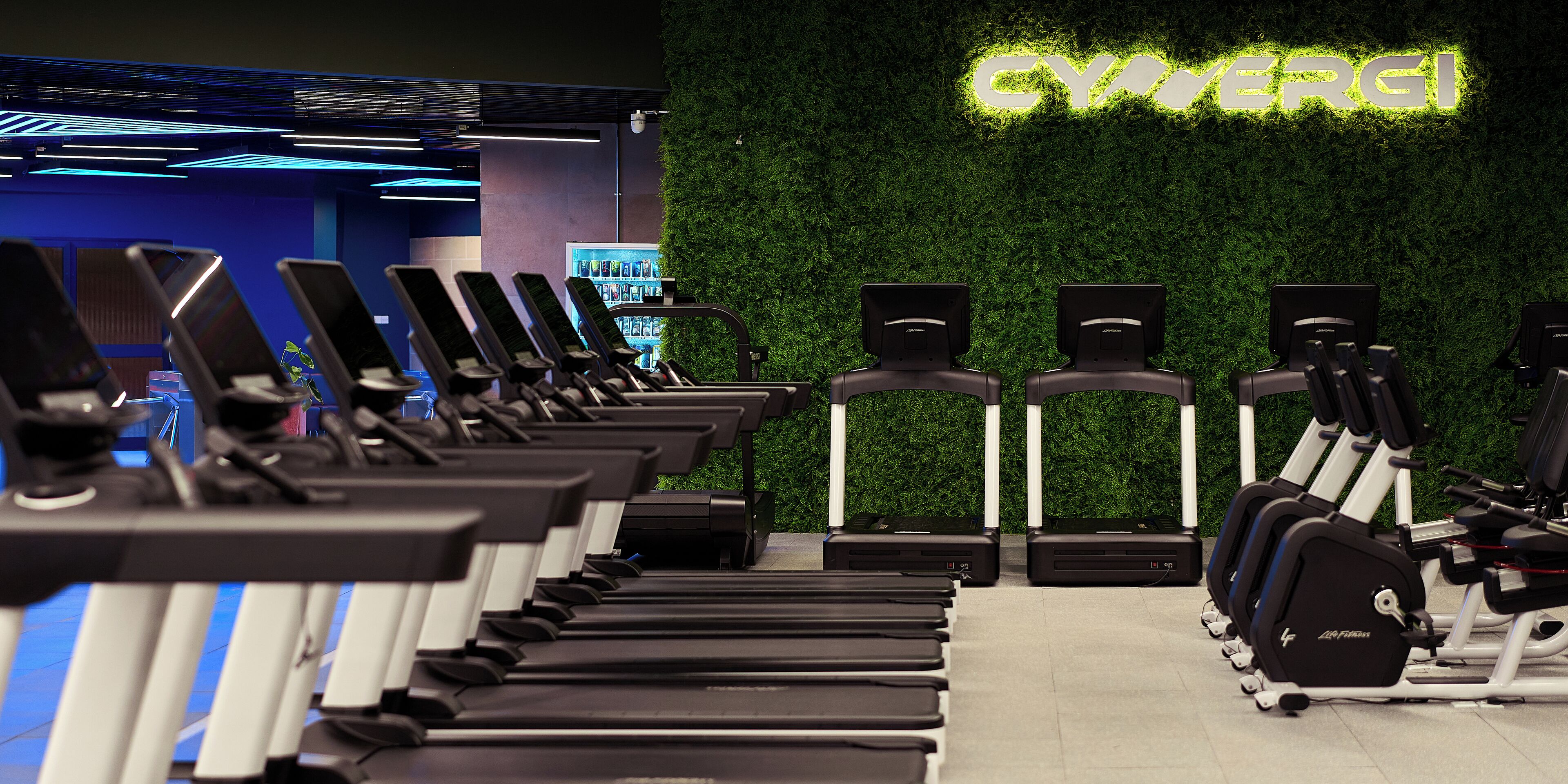 A gym with treadmills, weight machines, and a green wall with the word "GYM" illuminated.
