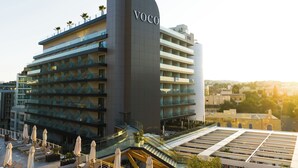 A modern hotel with a prominent 'Voco' sign, multiple balconies, and a rooftop terrace with sun loungers. - voco Malta by IHG (St. Julian's)