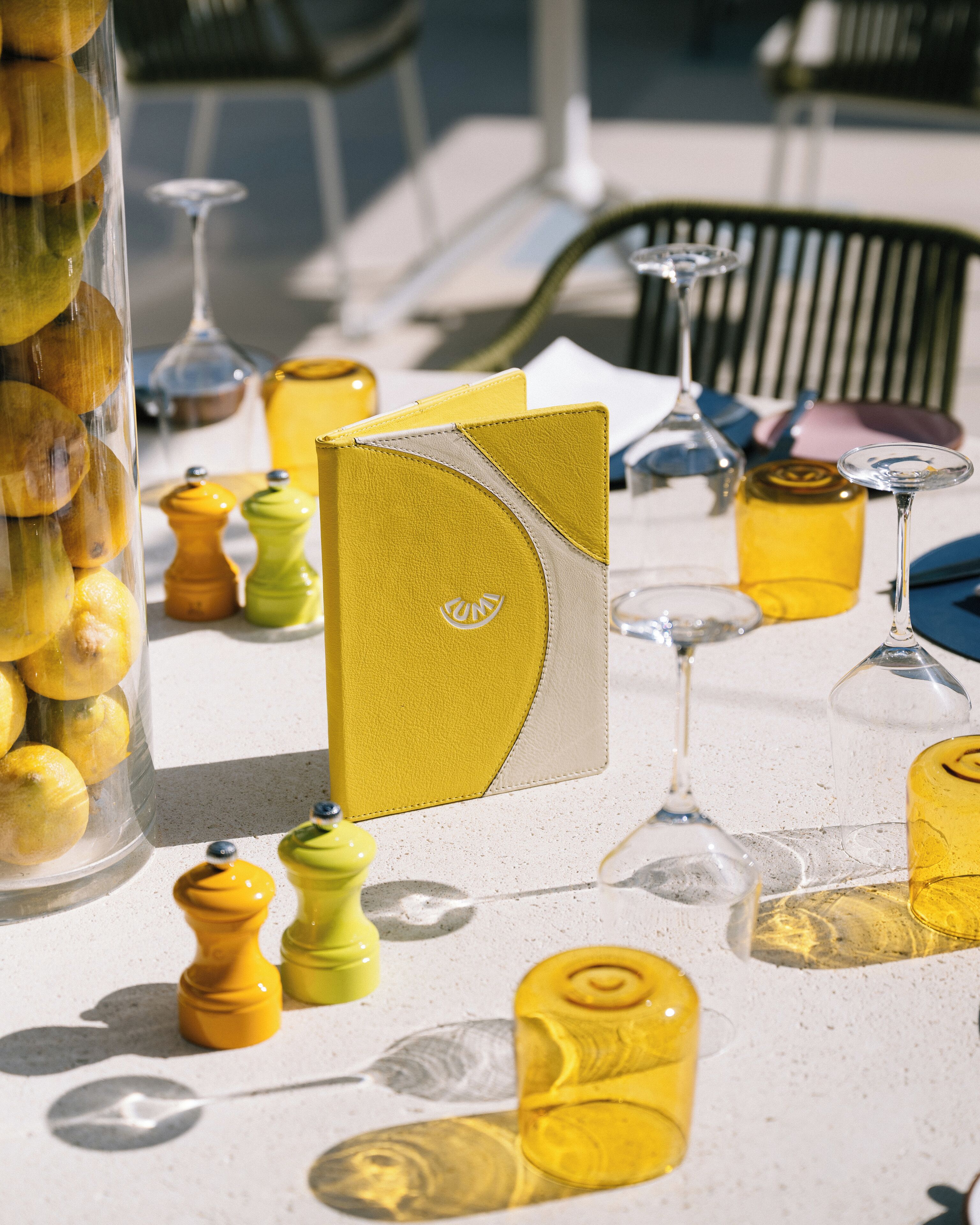 A table set with yellow and green salt and pepper shakers, a yellow notebook, and clear glassware.