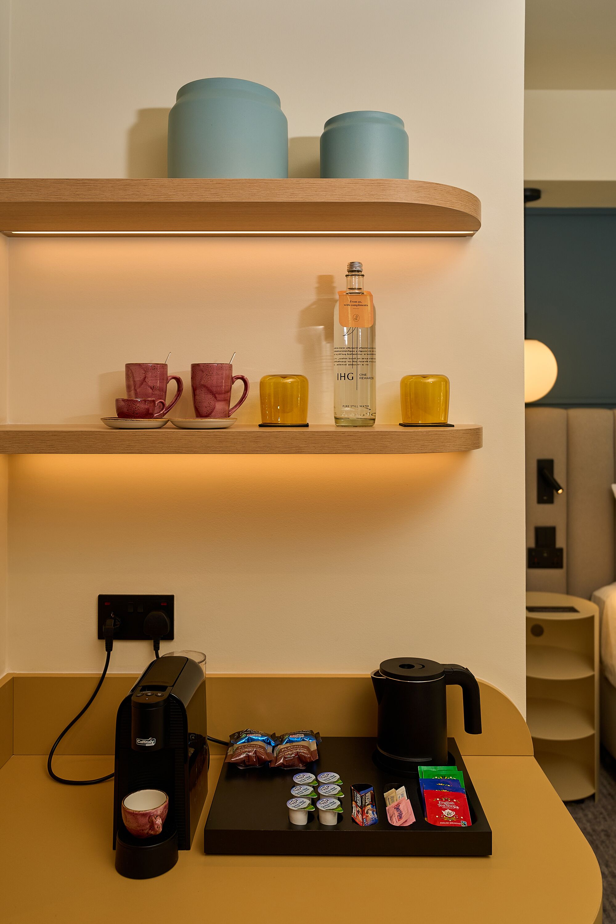 Una estación de café con una cafetera, tazas y cápsulas de café sobre una mesa.