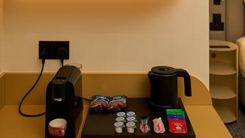 Una estación de café con una cafetera, tazas y cápsulas de café sobre una mesa.