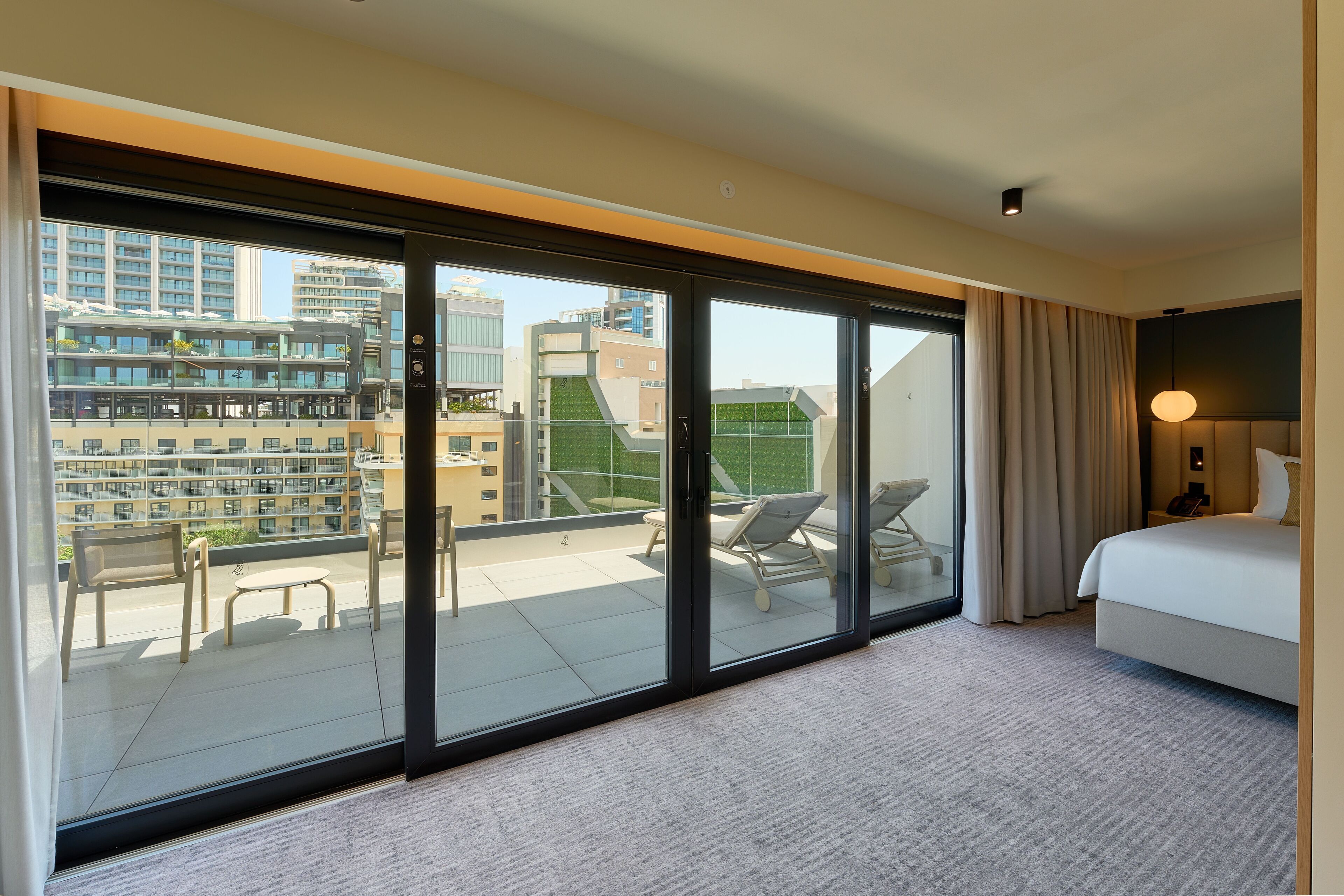 A hotel room with a large sliding glass door leading to an outdoor balcony, a bed, and a bedside table.