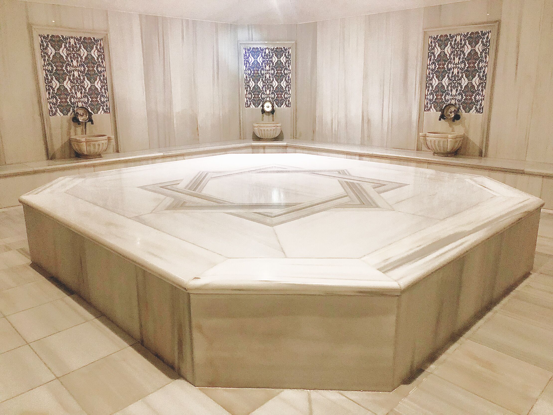 A large octagonal room with a central star-shaped design on the floor, surrounded by a high ceiling and patterned curtains.