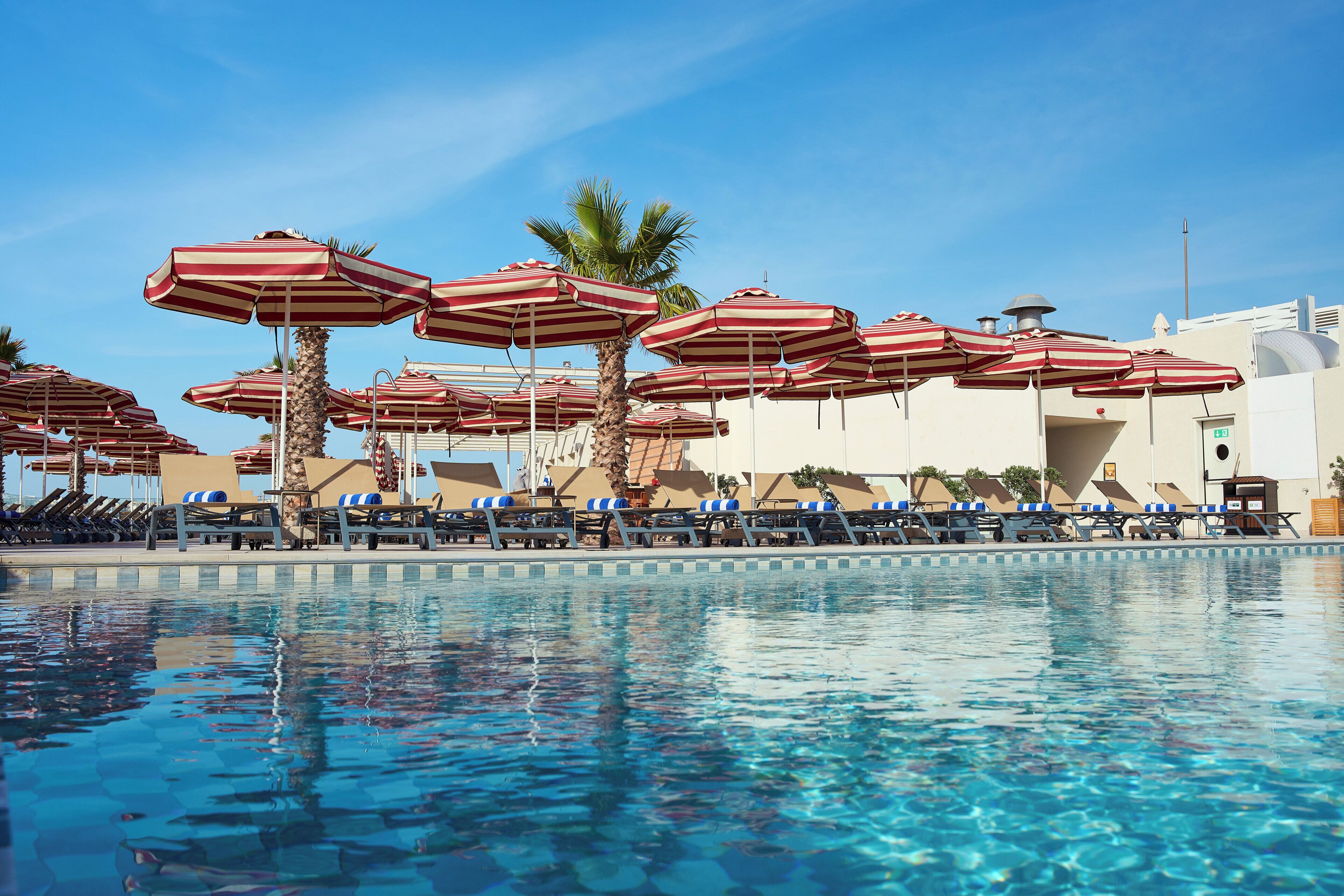 A pool area with multiple lounge chairs and striped umbrellas.
