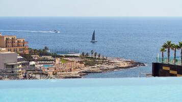 A coastal resort with a pool, beach umbrellas, and a sailboat on the water.