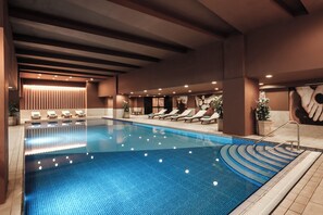 A large indoor swimming pool with lounge chairs and a modern ceiling design. - voco Malta by IHG (St. Julian's)
