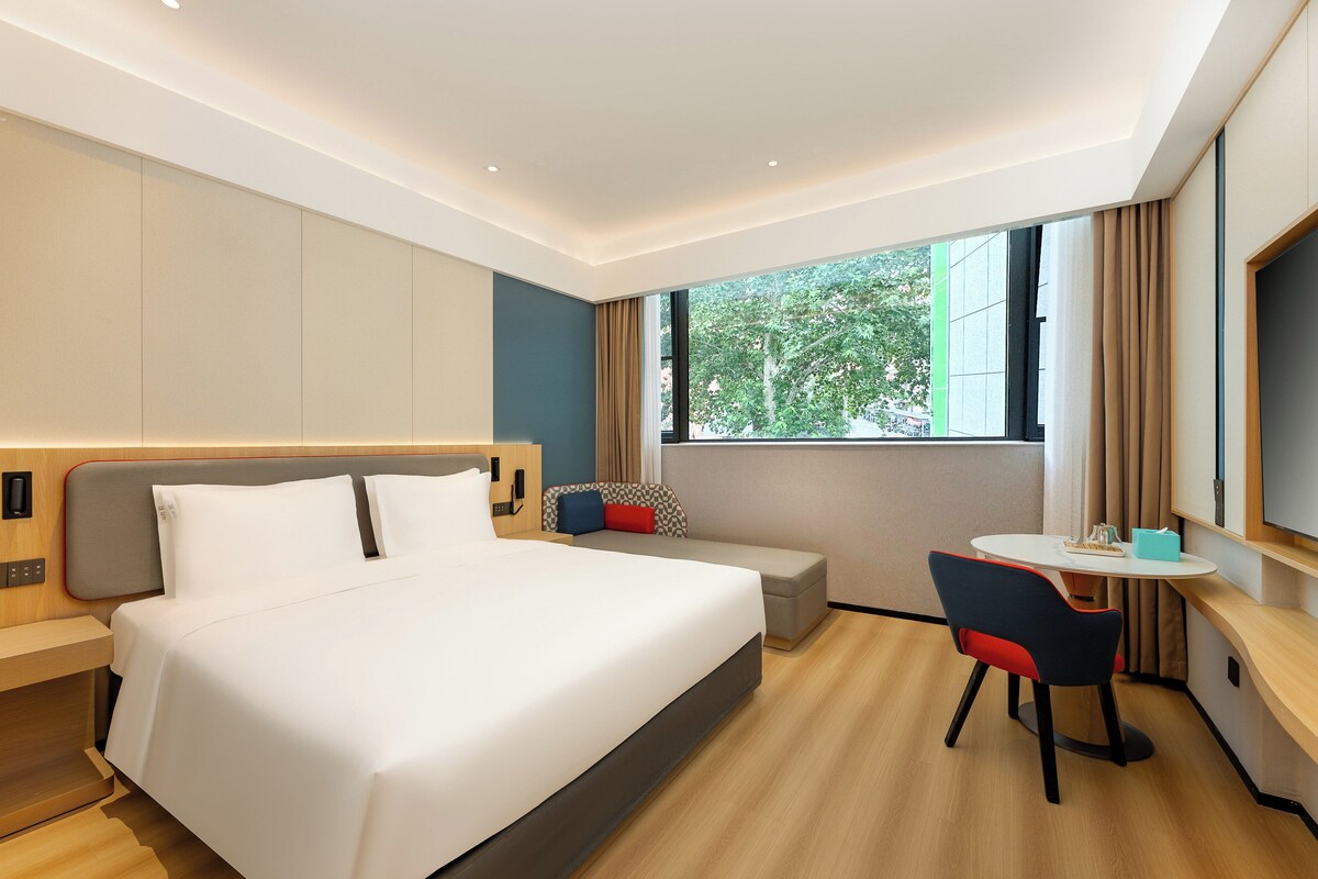 A modern hotel room with a large bed, a small desk, and a TV.