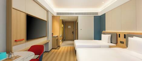 A hotel room with two beds, a desk with a chair, a TV, and a minibar.