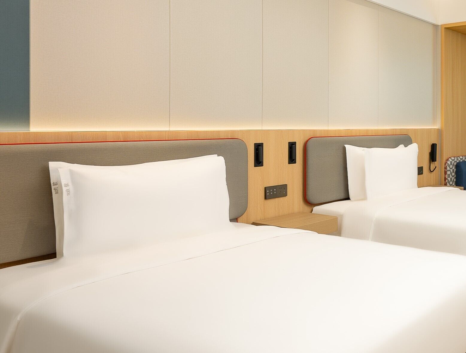 Habitación de hotel con dos camas, cabecero de madera, mesita de noche y teléfono en la pared.